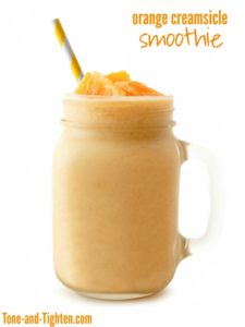 Orange smoothie in a mason jar glass with striped straw isolated on a white background